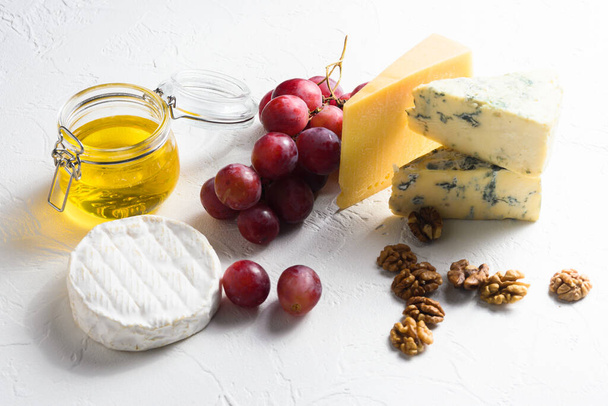 sortierte Käsesorten, Trauben, Nüsse vor weißem Hintergrund, italienischer und französischer Käse und Obstteller mit Honig und Wein. Seitenansicht. - Foto, Bild