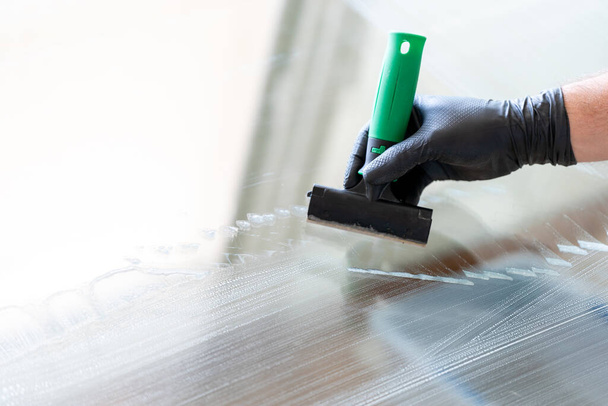 Um close de um cleaneer profissional usando um raspador de lâmina de diamante para limpar uma janela
 - Foto, Imagem