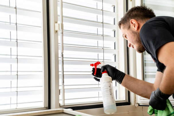 Un primer plano de un limpiador profesional limpiando persianas de ventana en un apartamento con un paño de micro fibra verde
 - Foto, imagen