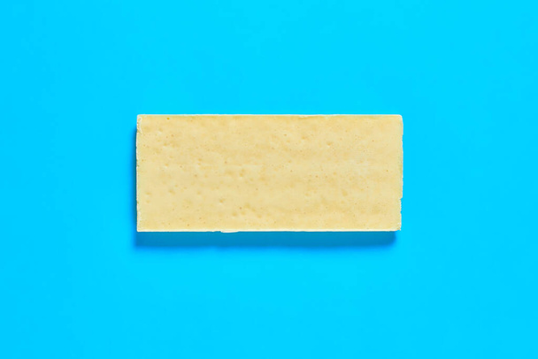 Single whole white porous chocolate bar lies on blue table on kitchen. Close-up - Φωτογραφία, εικόνα