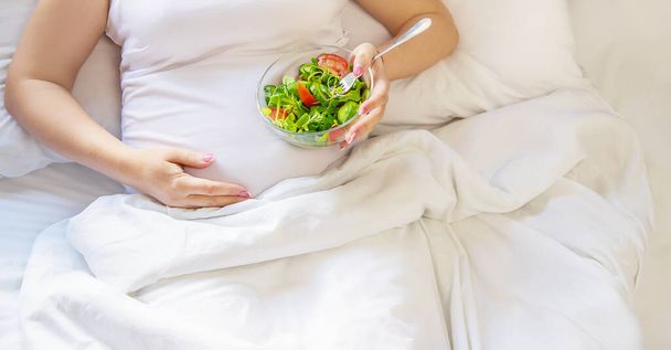Eine schwangere Frau isst einen Salat mit Gemüse. Selektiver Fokus. Lebensmittel. - Foto, Bild