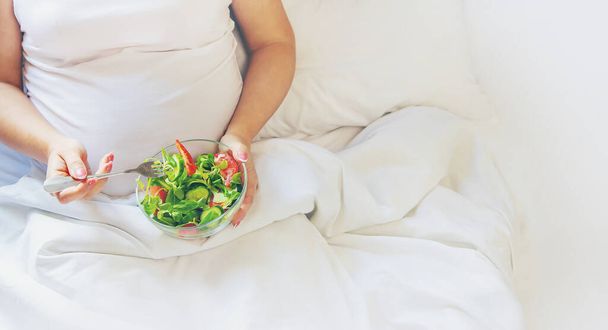 Een zwangere vrouw eet een salade met groenten. Selectieve focus. Voedsel. - Foto, afbeelding