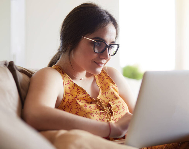junge Frau sitzt auf der Couch und arbeitet zu Hause am Laptop - Foto, Bild