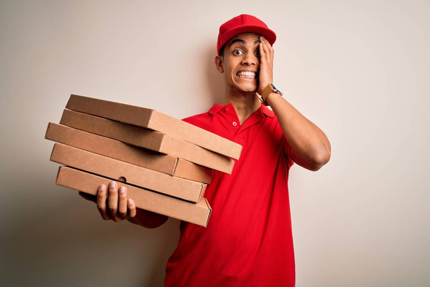 Handsome african american delivery man holding boxes of italian pizza over white background stressed with hand on head, shocked with shame and surprise face, angry and frustrated. Fear and upset for mistake. - Foto, Imagem