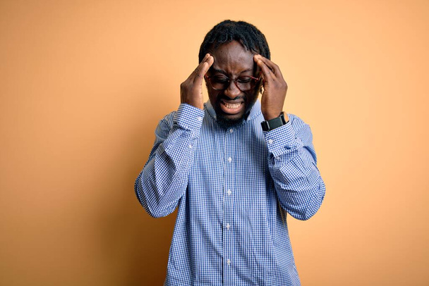 Mladý pohledný africký Američan nosí košili a brýle přes žluté pozadí s rukou na bolesti hlavy, protože stres. Trpící migréna. - Fotografie, Obrázek