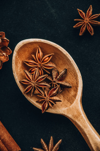wooden spoon with star anise on black background, christmas spices - Foto, afbeelding