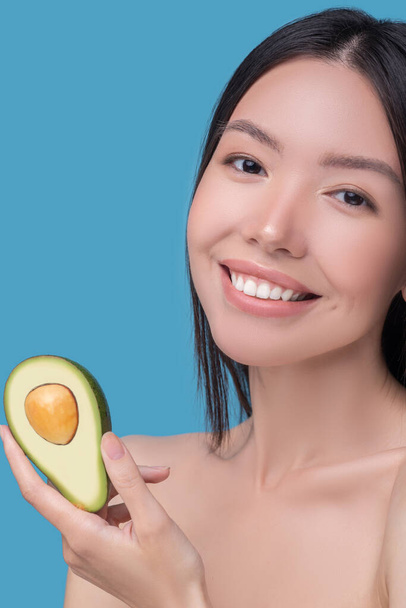 Smiling young asian woman holding avocado in her hands - Photo, image