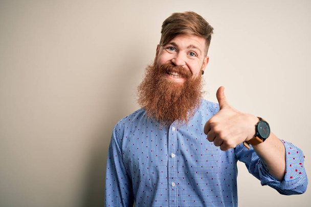 Beau roux irlandais homme d'affaires avec la barbe debout sur fond isolé faire des pouces heureux geste avec la main. Approuver l'expression en regardant la caméra montrant le succès
. - Photo, image