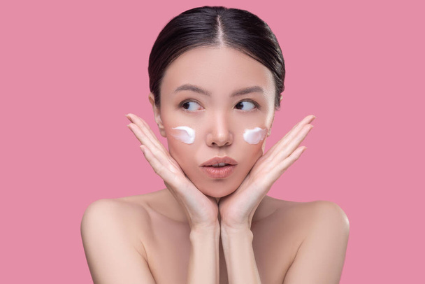 Pretty asian girl applying cream on her face - Foto, afbeelding