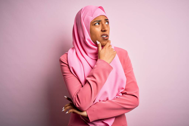 Junge afroamerikanische Afro-Frau trägt muslimischen Hijab über isoliertem rosa Hintergrund Denken besorgt über eine Frage, besorgt und nervös mit der Hand am Kinn - Foto, Bild