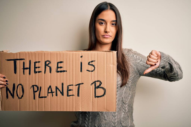Young beautiful brunette activist woman protesting for save the planet holding banner with fgry face, negative sign showing dislike with thumbs down, rejection concept - Photo, image