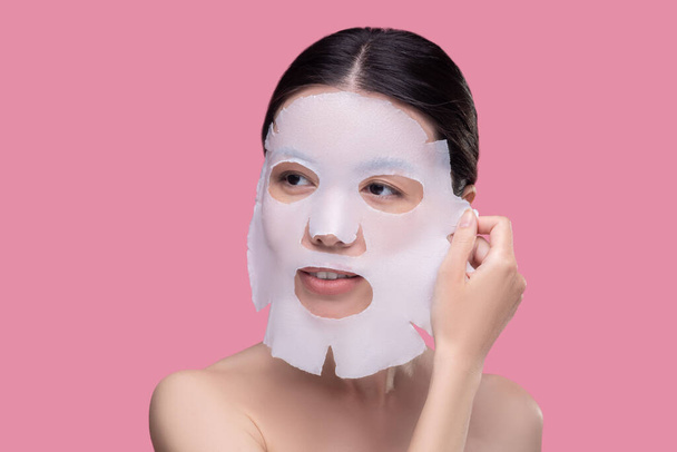 Dark-haired asian girl taking off the facial mask - Фото, изображение