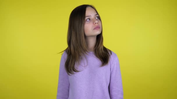 Teenager girl looks around and thinks what to choose on a yellow background - Video