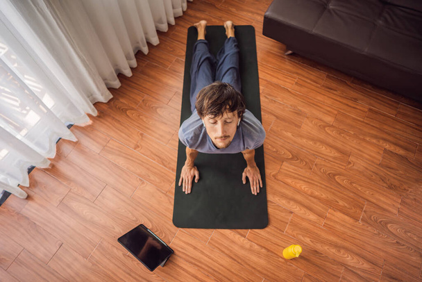 Hombre de fitness haciendo ejercicio en el suelo en casa y viendo videos de fitness en una tableta. La gente hace deportes en línea debido al coronovirus
 - Foto, Imagen