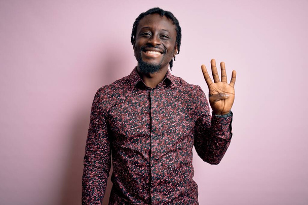 Giovane bell'uomo afro-americano che indossa una camicia casual in piedi su sfondo rosa mostrando e indicando con le dita il numero quattro mentre sorride fiducioso e felice
. - Foto, immagini