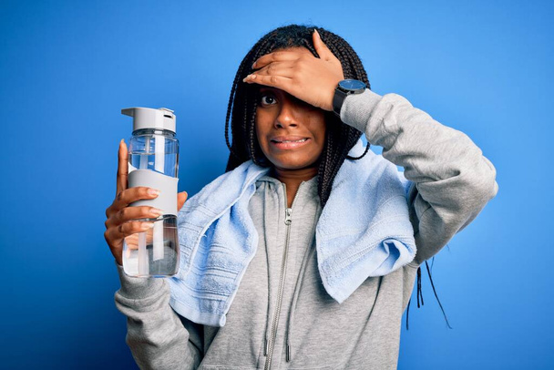 若いアフリカ系アメリカ人のスポーツ女性は、スウェットシャツを着て、水を飲んで頭の上に手で強調し、恥と驚きの顔でショックを受け、怒りと不満。恐怖と過ちへの動揺. - 写真・画像