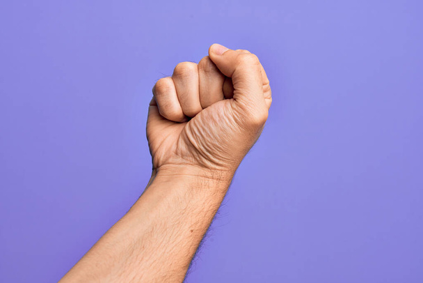 孤立した紫色の背景の上に指を示す白人青年の手は抗議と革命のジェスチャー、力と力を表現する拳を行う - 写真・画像