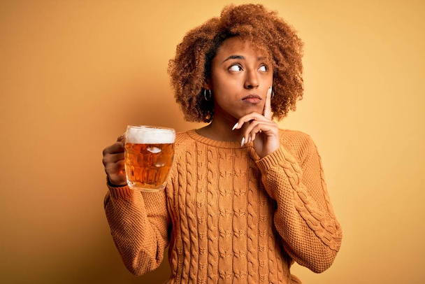 Jovem mulher afro afro afro afro bonita afro com cabelo encaracolado bebendo frasco de cerveja rosto sério pensando em questão, ideia muito confusa
 - Foto, Imagem
