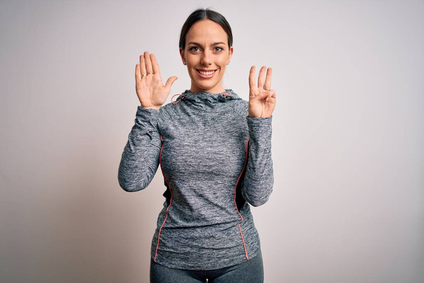 Giovane donna bionda fitness che indossa abiti sportivi su sfondo isolato mostrando e indicando con le dita il numero otto sorridendo fiducioso e felice
. - Foto, immagini