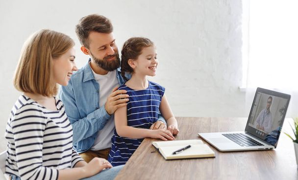 Pais modernos e filha alegre sentada à mesa e falando com o médico on-line no hom
 - Foto, Imagem