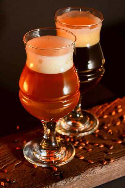 Two tulip beer glasses on dark wooden table over black background. Dark and light beer, stout beer, wheat beer. - Foto, imagen