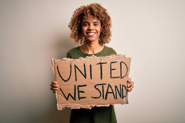 Africana attivista americana donna che chiede unità tenendo bandiera con unito stand messaggio con un volto felice in piedi e sorridente con un sorriso fiducioso che mostra denti - Foto, immagini