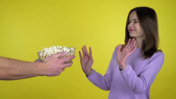 Teen girl in a pink sweater refuses popcorn in glass bowl shaking hands and head - Video