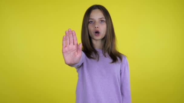 Adolescente chica levanta la mano con una palma y dice parada sobre fondo amarillo
 - Metraje, vídeo