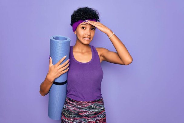 Young beautiful african american sporty woman wearing sportswear holding yoga mat stressed with hand on head, shocked with shame and surprise face, angry and frustrated. Fear and upset for mistake. - Foto, immagini