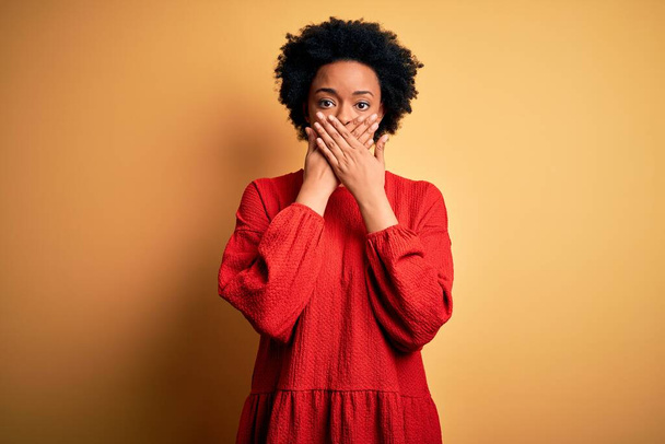 Young beautiful African American afro woman with curly hair wearing casual sweater shocked covering mouth with hands for mistake. Secret concept. - 写真・画像