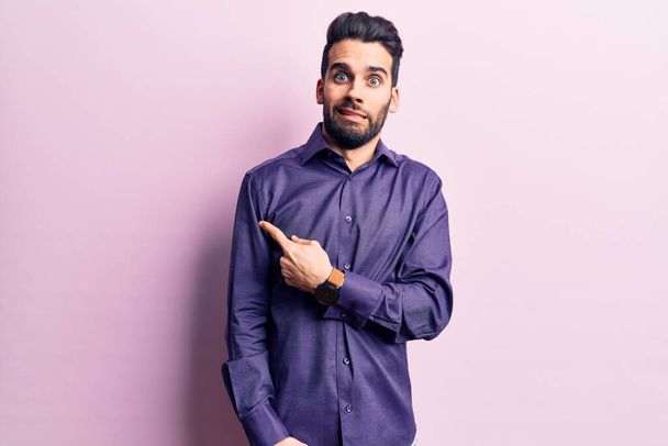 Young handsome man with beard wearing casual shirt pointing aside worried and nervous with forefinger, concerned and surprised expression  - Foto, Bild