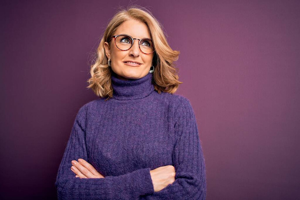 Middle age beautiful blonde woman wearing casual purple turtleneck sweater and glasses smiling looking to the side and staring away thinking. - Photo, Image