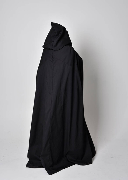 Portret kobiety w długim czarnym płaszczu. Pełnowymiarowa pozycja stojąca z tyłu do kamery, odizolowana na tle studia. - Zdjęcie, obraz