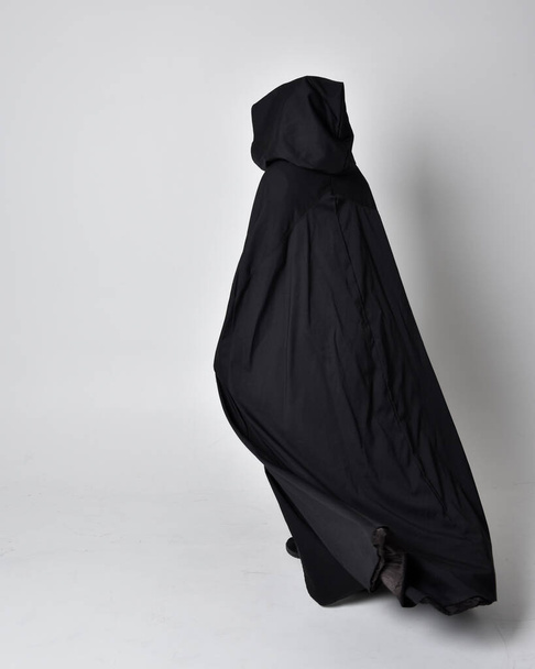 Portret kobiety w długim czarnym płaszczu. Pełnowymiarowa pozycja stojąca z tyłu do kamery, odizolowana na tle studia. - Zdjęcie, obraz
