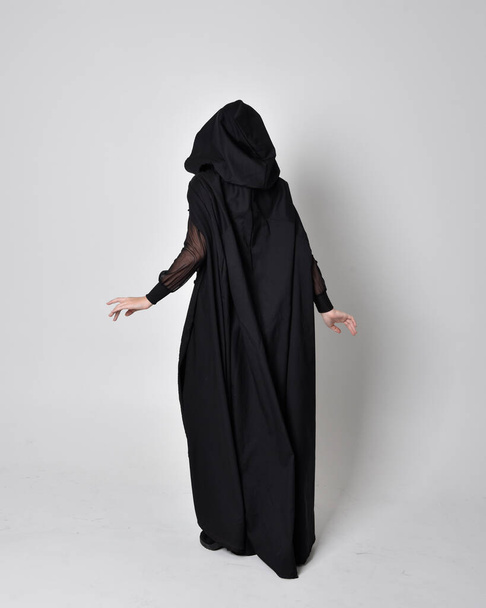 fantasy portrait of a woman wearing long black cloak. Full length standing pose  with back to the camera, isolated against a studio background. - Photo, Image