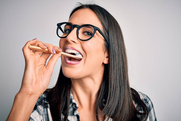 Jovem caucasiana usando óculos escovando os dentes usando escova de dentes e pasta oral, limpando dentes e língua como rotina da manhã de cuidados de saúde saudável
 - Foto, Imagem