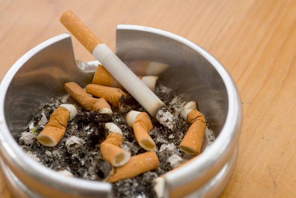 Cendrier plein de mégots de cigarette éteints avec un allumé
 - Photo, image