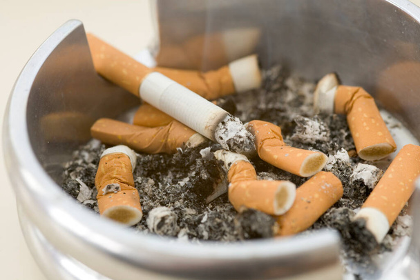 Cinzeiro cheio de pontas de cigarro extintas com um aceso
 - Foto, Imagem