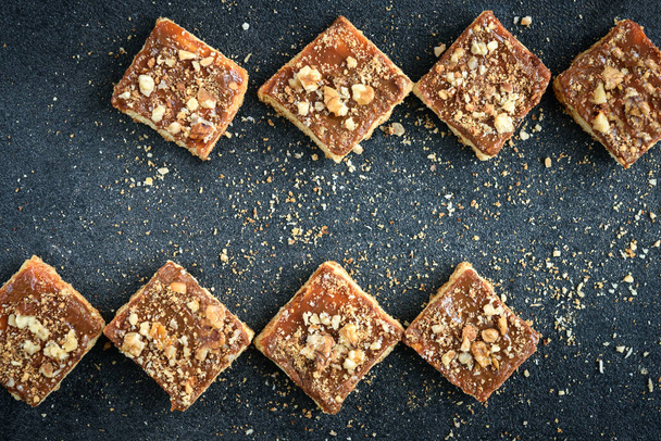 Caramel maison sablé carrés biscuits avec des noix posées sous la forme d'un carré sur fond noir avec des miettes
. - Photo, image