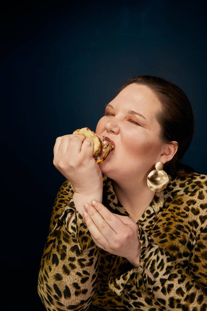 The concept of gluttony. Overweight. Fat woman does not eat hamburger appetizingly. - Zdjęcie, obraz