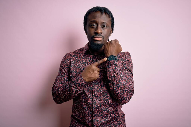 Young handsome african american man wearing casual shirt standing over pink background In hurry pointing to watch time, impatience, looking at the camera with relaxed expression - Foto, Imagem