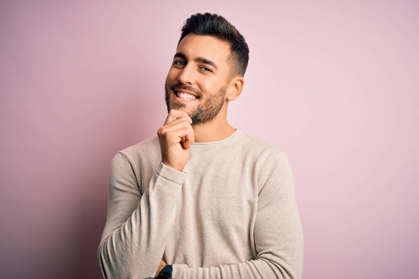 Young handsome man wearing casual sweater standing over isolated pink background looking confident at the camera with smile with crossed arms and hand raised on chin. Thinking positive. - Fotó, kép