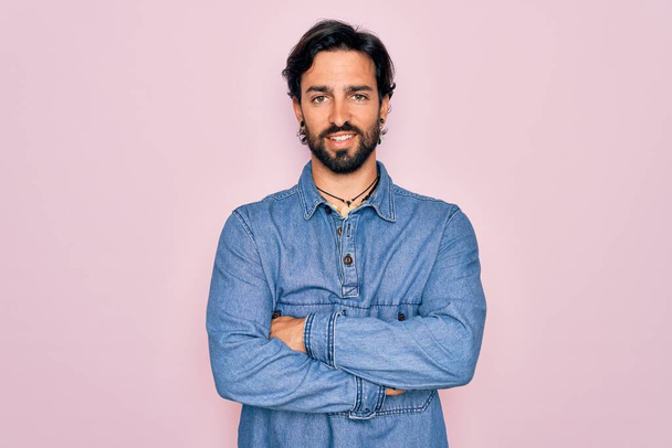 Fiatal jóképű spanyol bohém férfi hippi stílusban rózsaszín háttér felett boldog arc mosolyogva keresztbe tett karokkal nézi a kamerát. Pozitív személy. - Fotó, kép