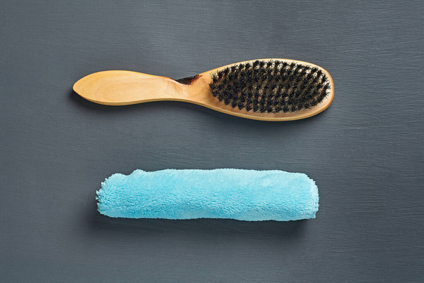 One inverted brush with wooden handle for cleaning clothes or footwear near rolled blue towel lies on dark concrete desk in bathroom. Close-up. Top view - Foto, Imagem
