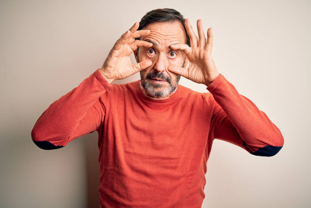 Middle age hoary man wearing casual orange sweater standing over isolated white background Trying to open eyes with fingers, sleepy and tired for morning fatigue - Zdjęcie, obraz