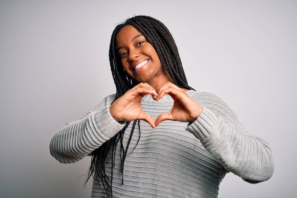 Jonge Afro-Amerikaanse vrouw staat casual en koel over grijs geïsoleerde achtergrond glimlachen in liefde tonen hart symbool en vorm met de handen. Romantisch concept. - Foto, afbeelding