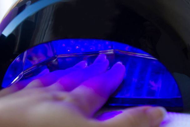 Detailní záběr na ruku ženy uvnitř UV lampy, vytvrzující její nedávno nanesený gel na nehty šelak doma. Domácí police péče o nehty koncept - Fotografie, Obrázek