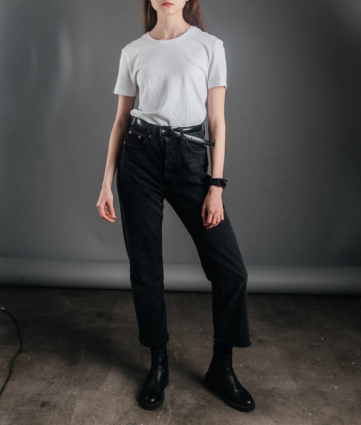 poseren. model meisje poseren in zwarte jeans met een hoge taille en een riem, een wit T-shirt. poserende lessen. fotosessie in de studio. vrouwelijke poses - Foto, afbeelding