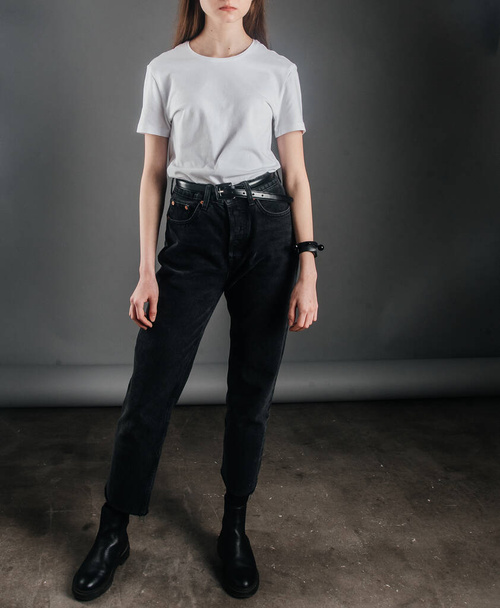 позирует. Девушка-модель позирует в черных джинсах с высокой талией и поясом, белой футболкой. уроков позирования. фотосессия в студии. позы женщин
 - Фото, изображение