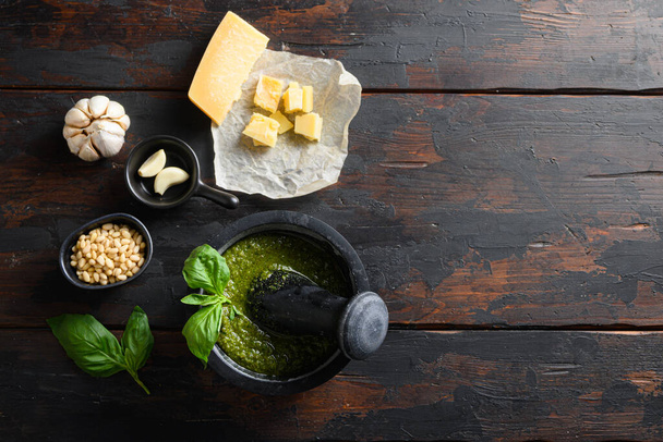 fresh Green basil pesto preparation in black mortar with italian recipe ingredients over old wood table copy space for text overhead - Photo, image